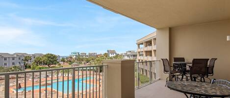 A balcony with a pool view, outdoor furniture, and a clear sky.