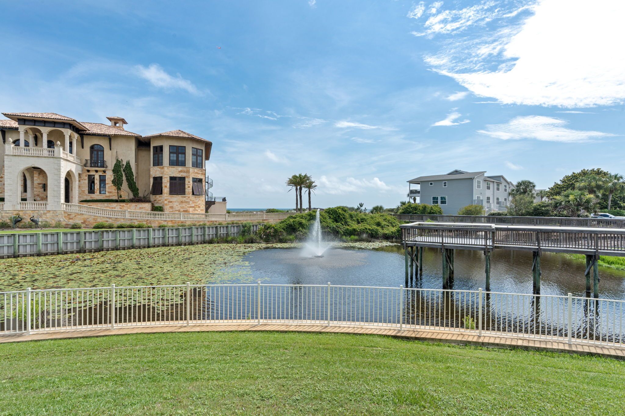 A large house with a fountain, a pond, and a bridge.