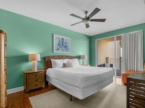 A bedroom with a bed, two bedside tables with lamps, a ceiling fan, a large window, and a sliding glass door leading to a balcony. - Gulf and Pool Views, Free Seasonal Beach Service, Designated Beach Area on 30A!! (Santa Rosa Beach)