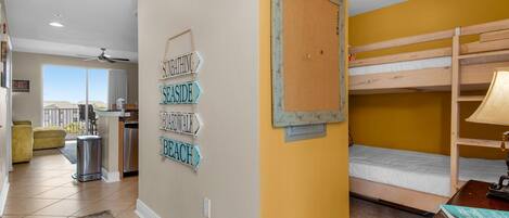A room with a bunk bed, a corkboard with directional signs, a kitchen area, and a view to the outside.