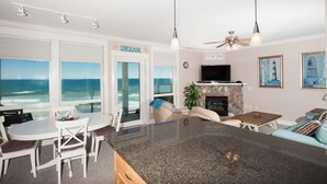 Een ruime woonkamer met een groot raam met uitzicht op de oceaan, een open haard en een televisie.