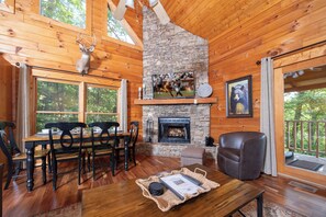A log cabin interior with a stone fireplace, wooden dining table, and a leather chair.