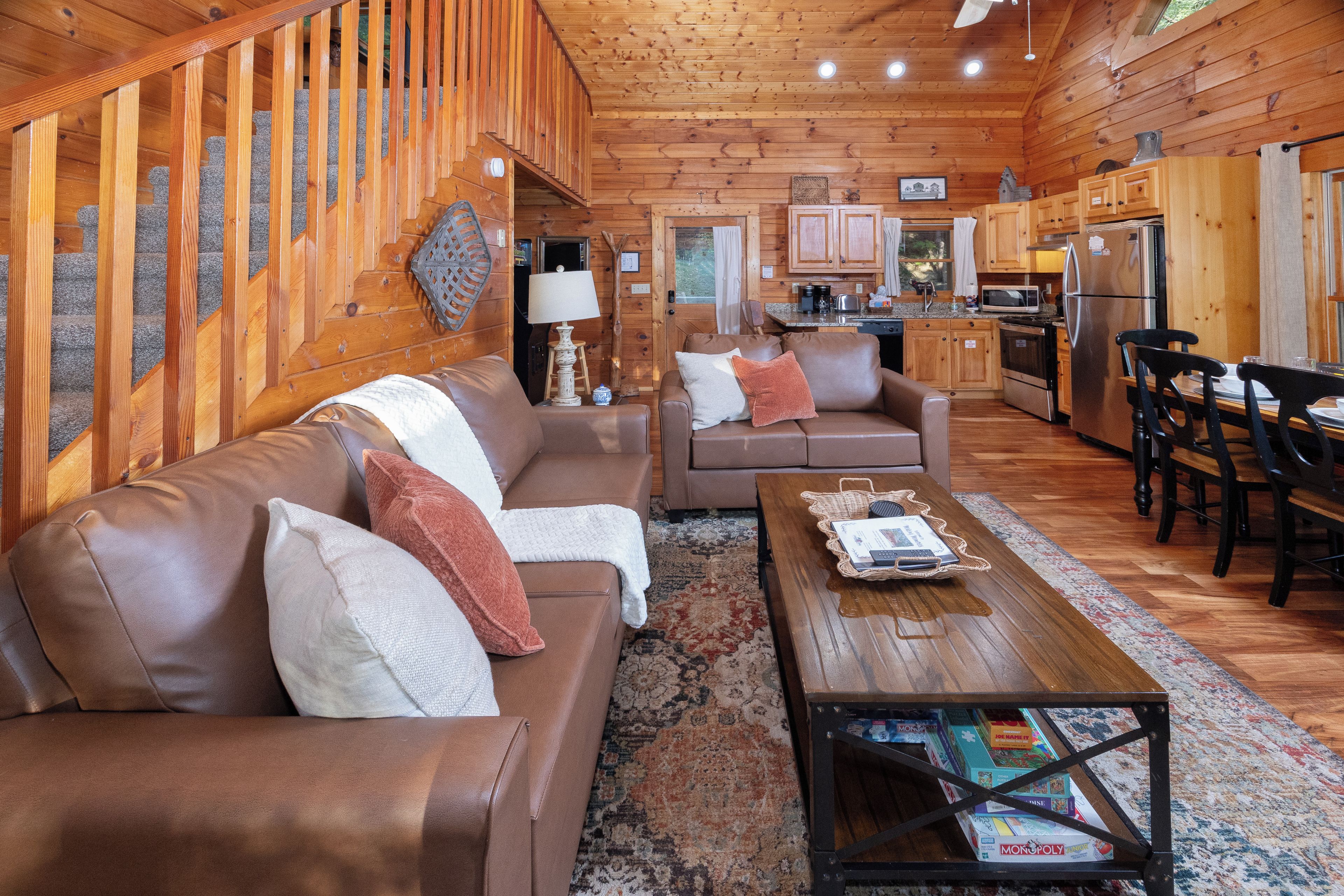 Ein gemütliches Blockhaus-Interieur mit Holzvertäfelung, einem Wohnzimmer mit Sofa und Sesseln, einer Essecke mit Tisch und Stühlen sowie einer Küche mit modernen Geräten.