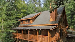 Eine Blockhütte mit Balkon, umgeben von dichtem Wald.