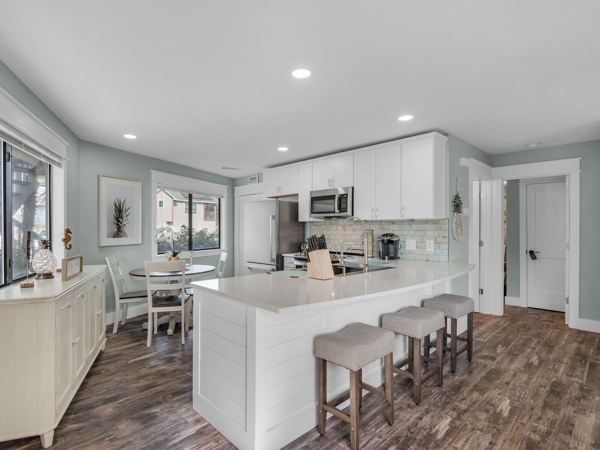 A modern kitchen with white cabinetry, a central island with bar stools, and a dining area with a table and chairs.
