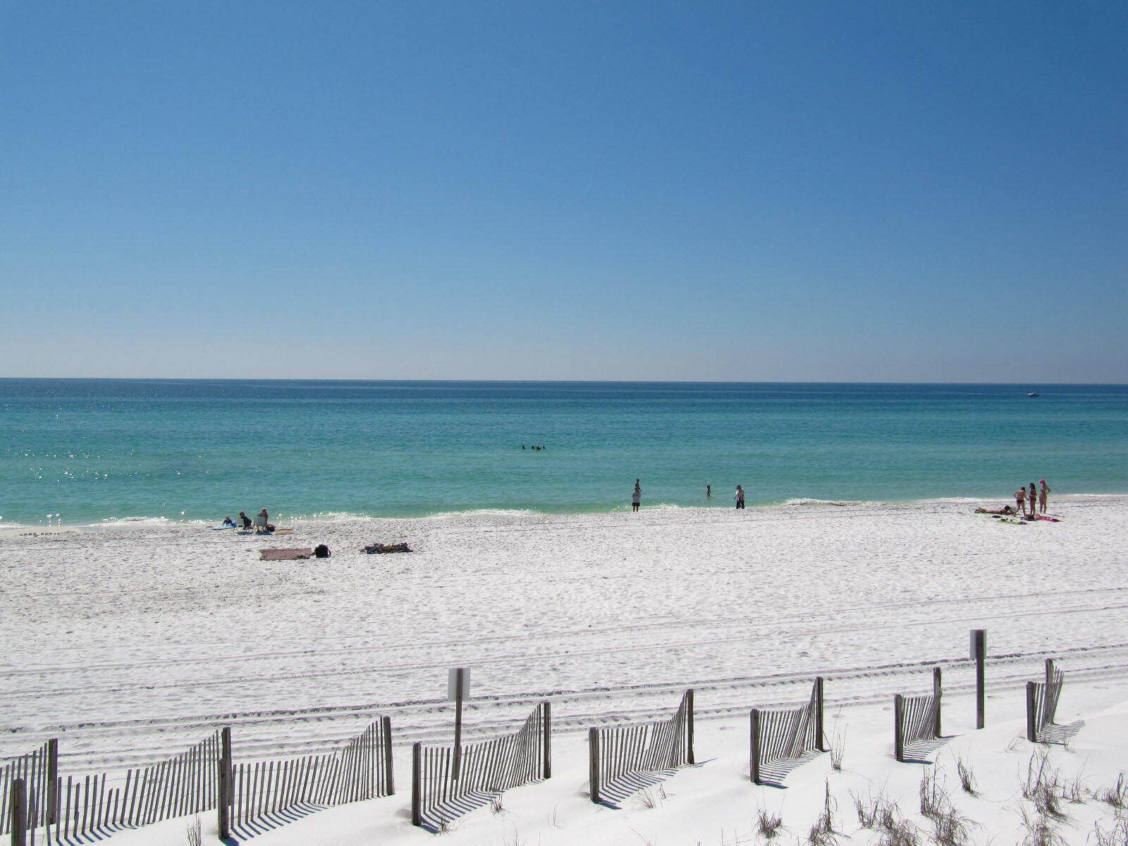A beach with a sandy shore, a clear blue sky, and a calm sea.