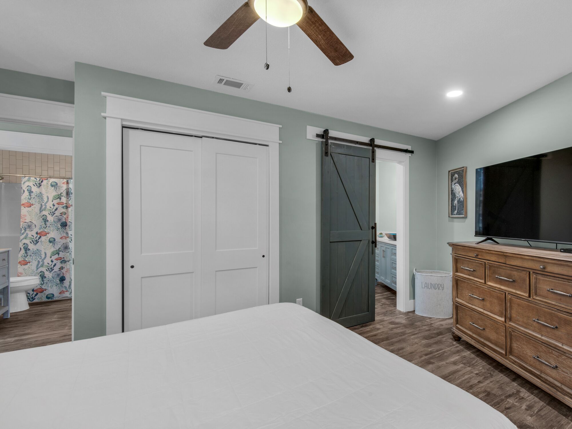 A bedroom with a bed, a dresser, a TV, and a ceiling fan.