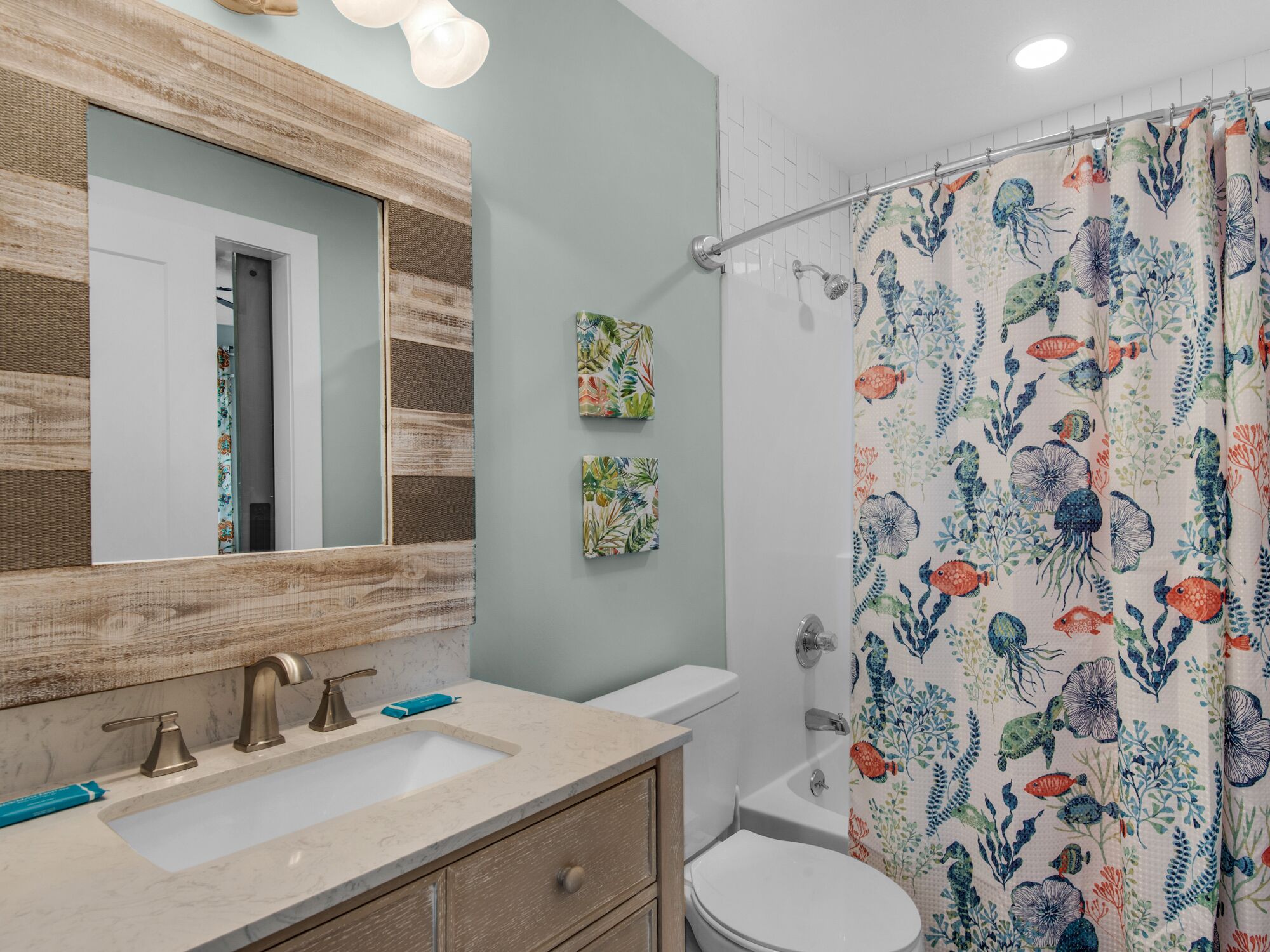 Une salle de bain avec un meuble-lavabo en bois, un évier, des toilettes et un rideau de douche orné de motifs représentant la vie marine.