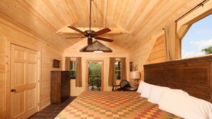Ein Schlafzimmer einer Holzhütte mit einem großen Bett, Deckenventilator und Blick durch ein Fenster.