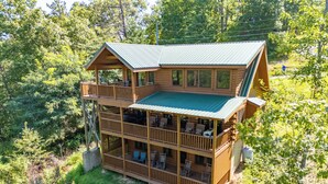 Eine zweistöckige Blockhütte mit einem Balkon im Obergeschoss, umgeben von dichtem Wald.