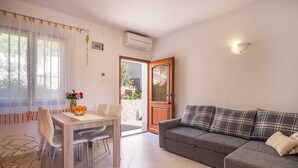 A modern living room with a grey sofa, a dining table with chairs, and a view of the garden through an open door. - Apartment IVA with a sea view (Krk)
