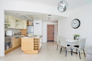 A modern kitchen with a central island, white cabinetry, and a dining area with two chairs.