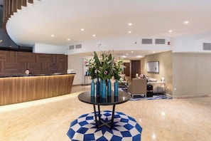 A hotel lobby with a reception desk, a round table with vases, and a staircase.