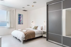A modern bedroom with a bed, bedside tables, a window with curtains, a painting on the wall, and a sliding door.