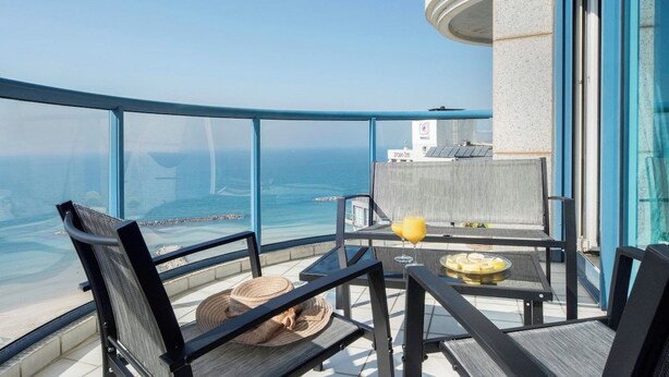 En balkon med havudsigt, et bord med et glas appelsinjuice og en stol med en vævet måtte.