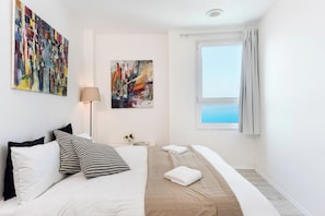 A hotel room with a bed, a window with curtains, and two paintings on the wall.
