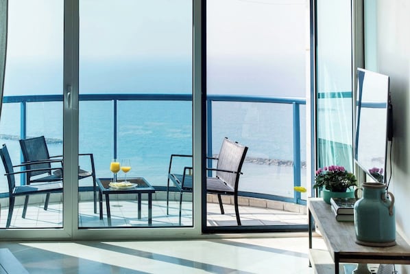 Un balcón con vistas al mar, amueblado con sillas y una mesa, y un jarrón con flores.