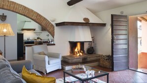 A cozy living room with a fireplace, a dining area, and a kitchen visible through an archway. - Montestigliano, an authentic farmhouse in the heart of Tuscany, is an oasis of peace and beauty that offers its guests refined residences and an enchanting view (Rosia - Sovicille)