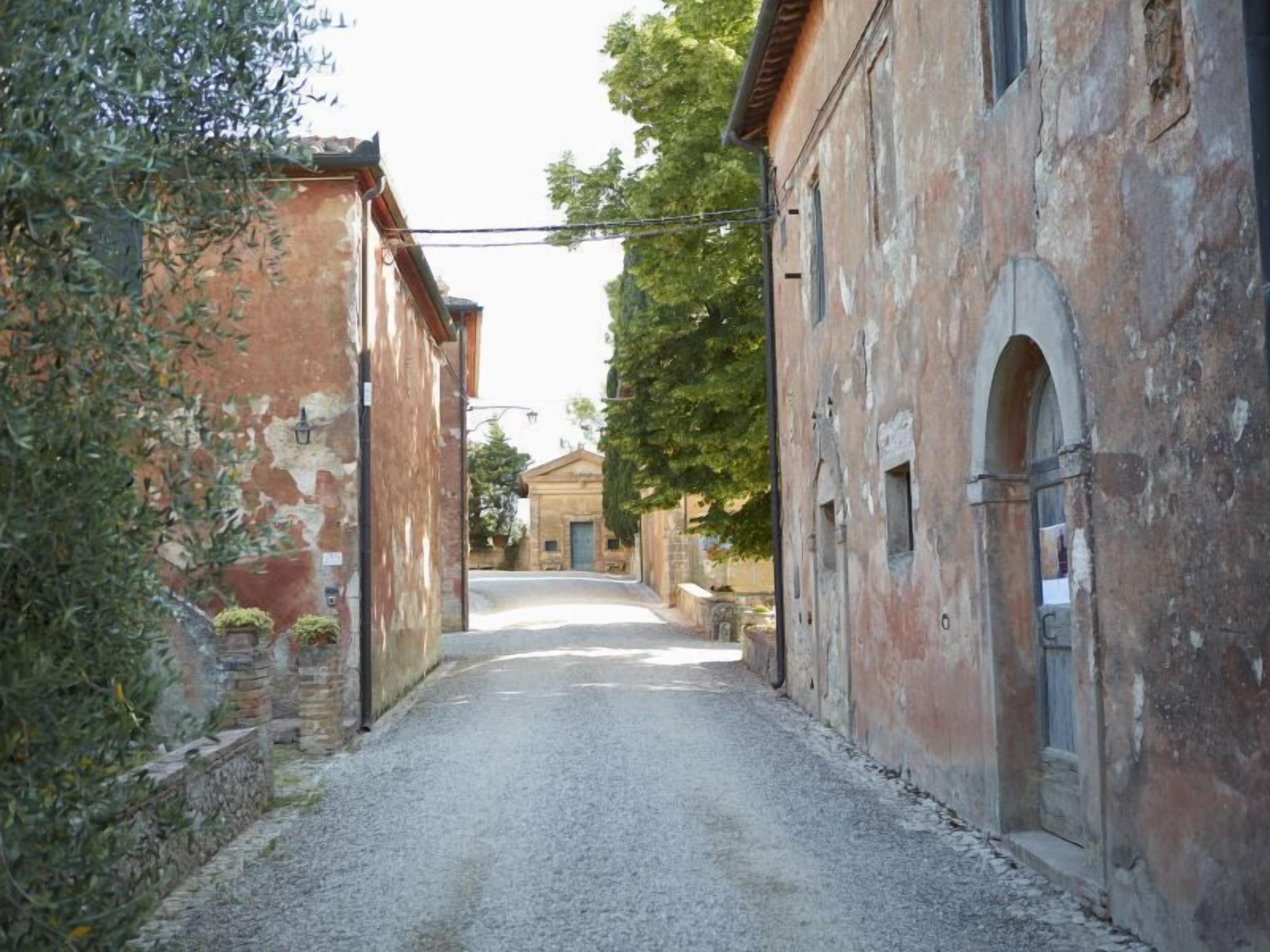 Eine enge Kopfsteinpflasterstraße, gesäumt von alten Gebäuden mit Rundbogenportalen, und in der Ferne ein kleines Haus.