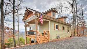 Une cabane à deux étages, dotée d’un porche et d’un escalier en bois, entourée d’arbres et bordée d’une allée en gravier.