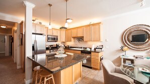 A modern kitchen with granite countertops, stainless steel appliances, wooden cabinets, and a central island with stools. - Promo! Oceanfront Condo - Private Hot Tub, WiFi, HDTV and Pool! (Lincoln City)