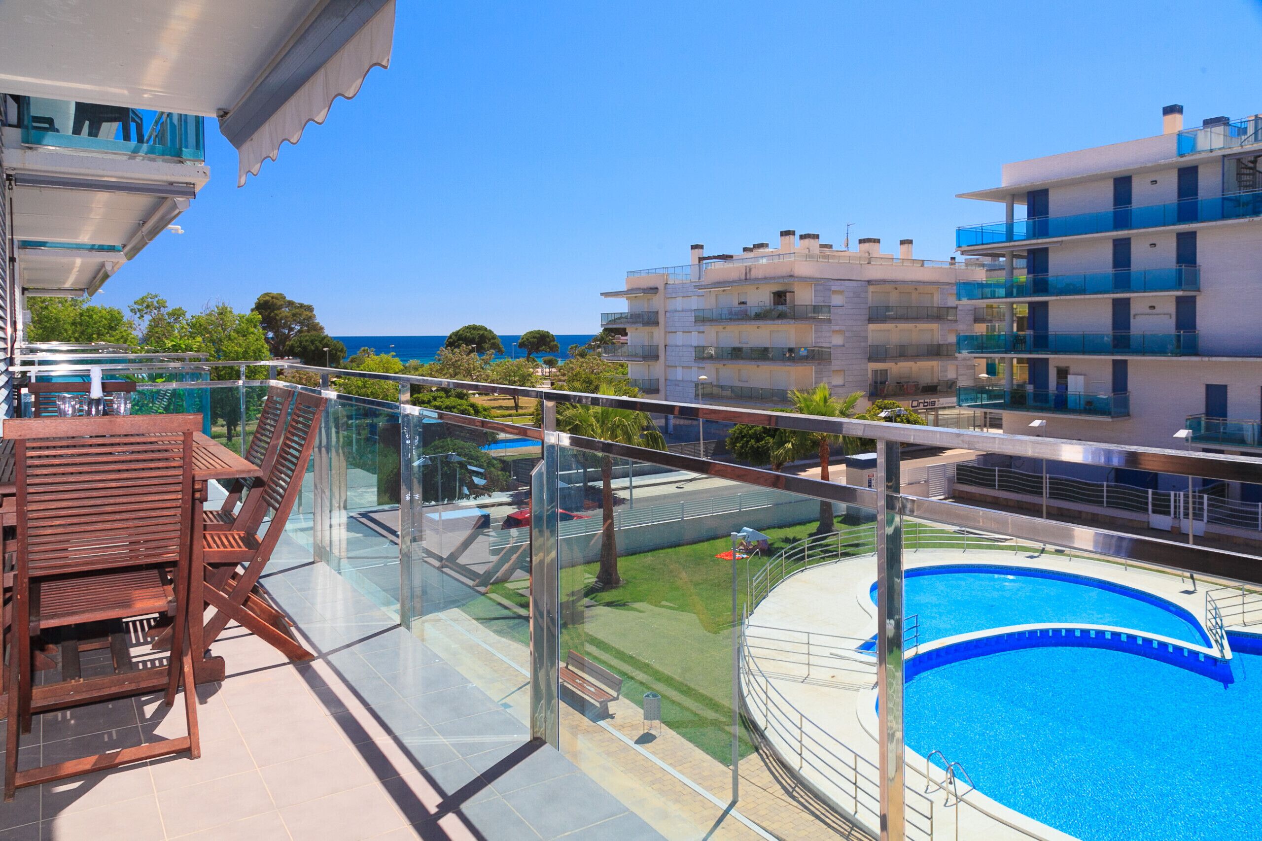 Un balcón con barandilla de vidrio que da a una piscina y ofrece vistas despejadas al mar.