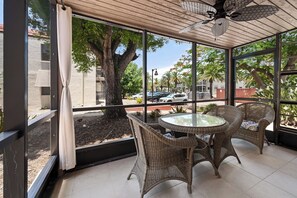 Un patio techado con mobiliario de mimbre, una mesa de vidrio y un ventilador de techo.
