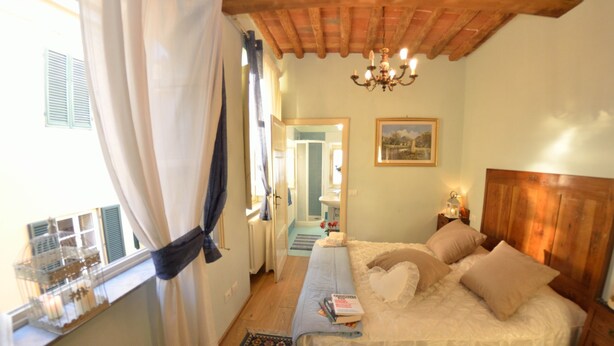 A bedroom with a bed, a nightstand, a chandelier, a window with curtains, and a view of the bathroom. - Apartment in Lucca with 3 bedrooms sleeps 7 (Lucca)