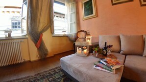 A cozy living room with a sofa, a table with books and a bottle, a decorative birdcage with candles, and a view of the outside through a window. - Apartment in Lucca with 3 bedrooms sleeps 7 (Lucca)