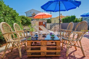 An outdoor dining area with wicker chairs and a glass table, surrounded by potted plants and a stone wall.