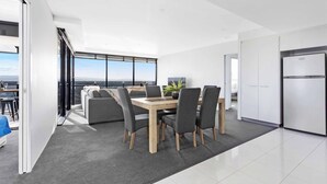 A modern kitchen with a built-in refrigerator, a dining area with a wooden table and grey chairs, and a large window offering a view of the city. - Circle on Cavill River View (Surfers Paradise)