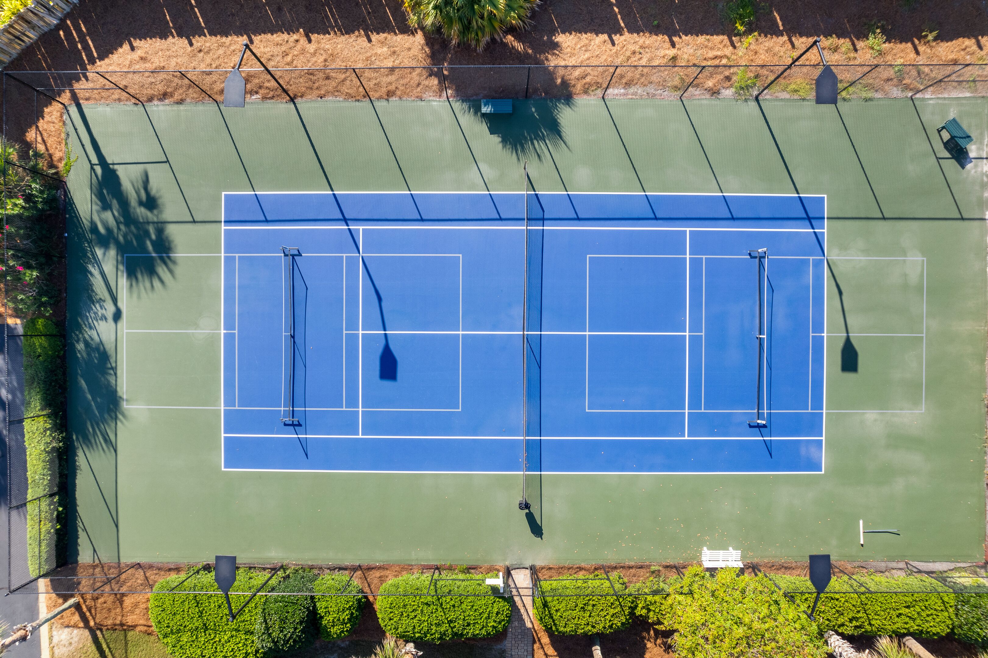 An aerial view of a tennis court with two courts, surrounded by a fence and greenery.