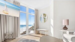 A modern room with a large window, a round mirror, a bench, and a lamp. - Gulf Front Balcony, Gorgeous Views, Near Destin Harbor (Destin)