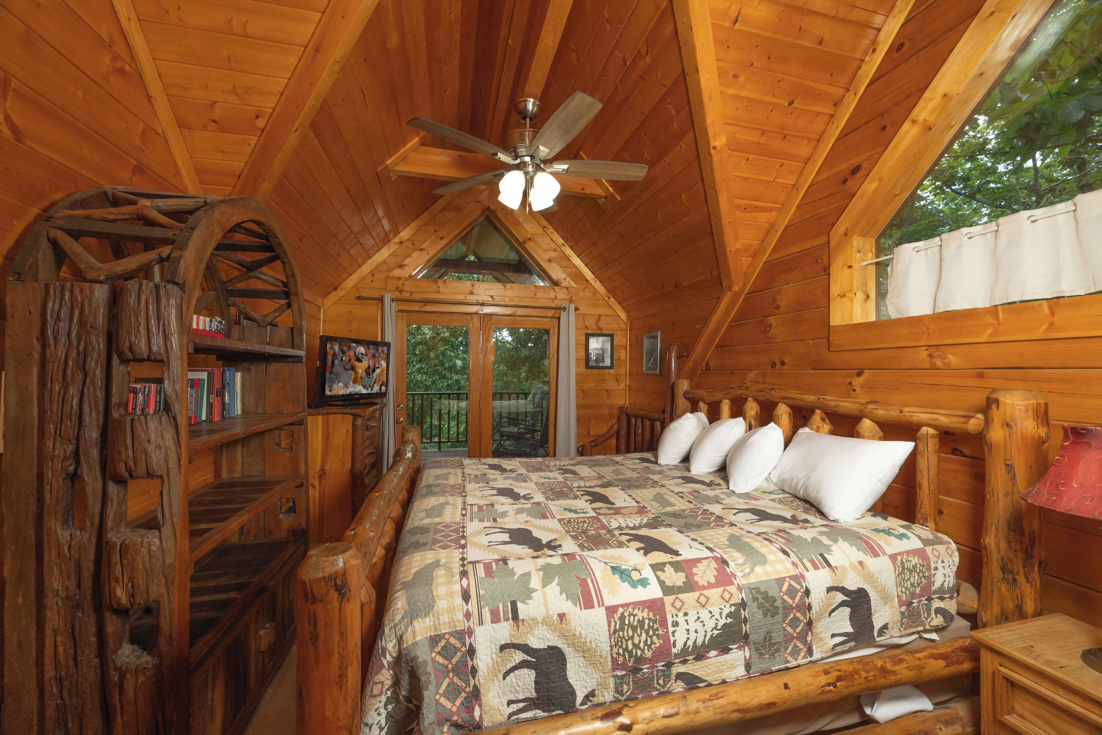 Un dormitorio de cabaña de madera con una cama grande, un ventilador de techo, estanterías de madera y una estructura de rueda de madera rústica.