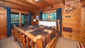 Un dormitorio de cabaña de madera con una cama grande, paredes de madera y ventana con vistas al bosque.