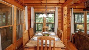 Un comedor de madera con una mesa dispuesta para cuatro, rodeado de paredes de madera y ventanas amplias.