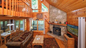Un interior de cabaña acogedor con una zona de comedor de madera, una chimenea y un ventanal grande con vistas al bosque.