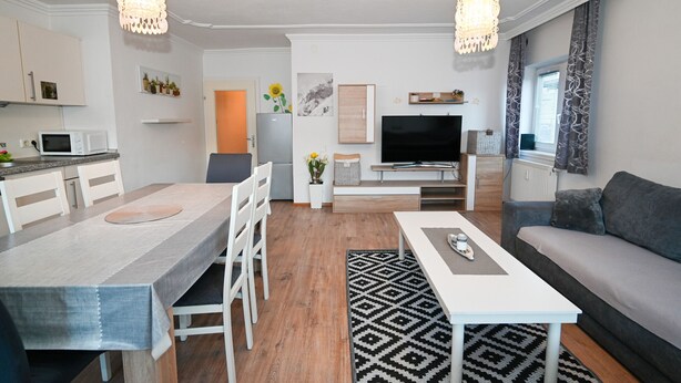 Moderni olohuone, jossa on sohva, ruokapöytä tuoleineen, televisio ja keittiöalue, jossa on mikroaaltouuni.