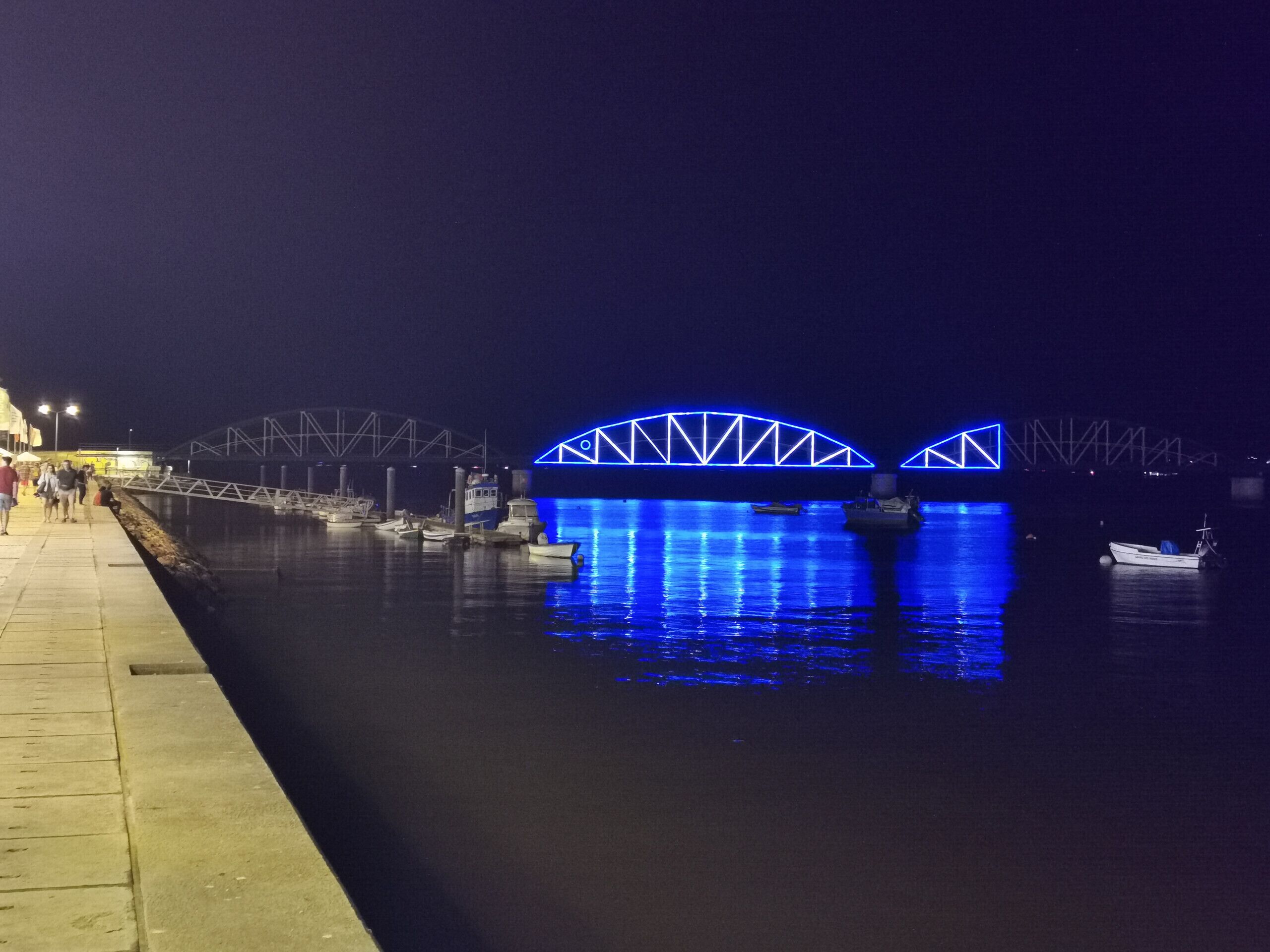 A nighttime view of a river with illuminated bridges and boats docked along the shore.