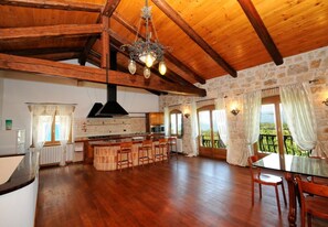 A spacious kitchen with a central island, wooden beams, stone walls, and a large window offering a view. - Villa Carla | Istrian Stone Villa with Sea View (Vrsar)