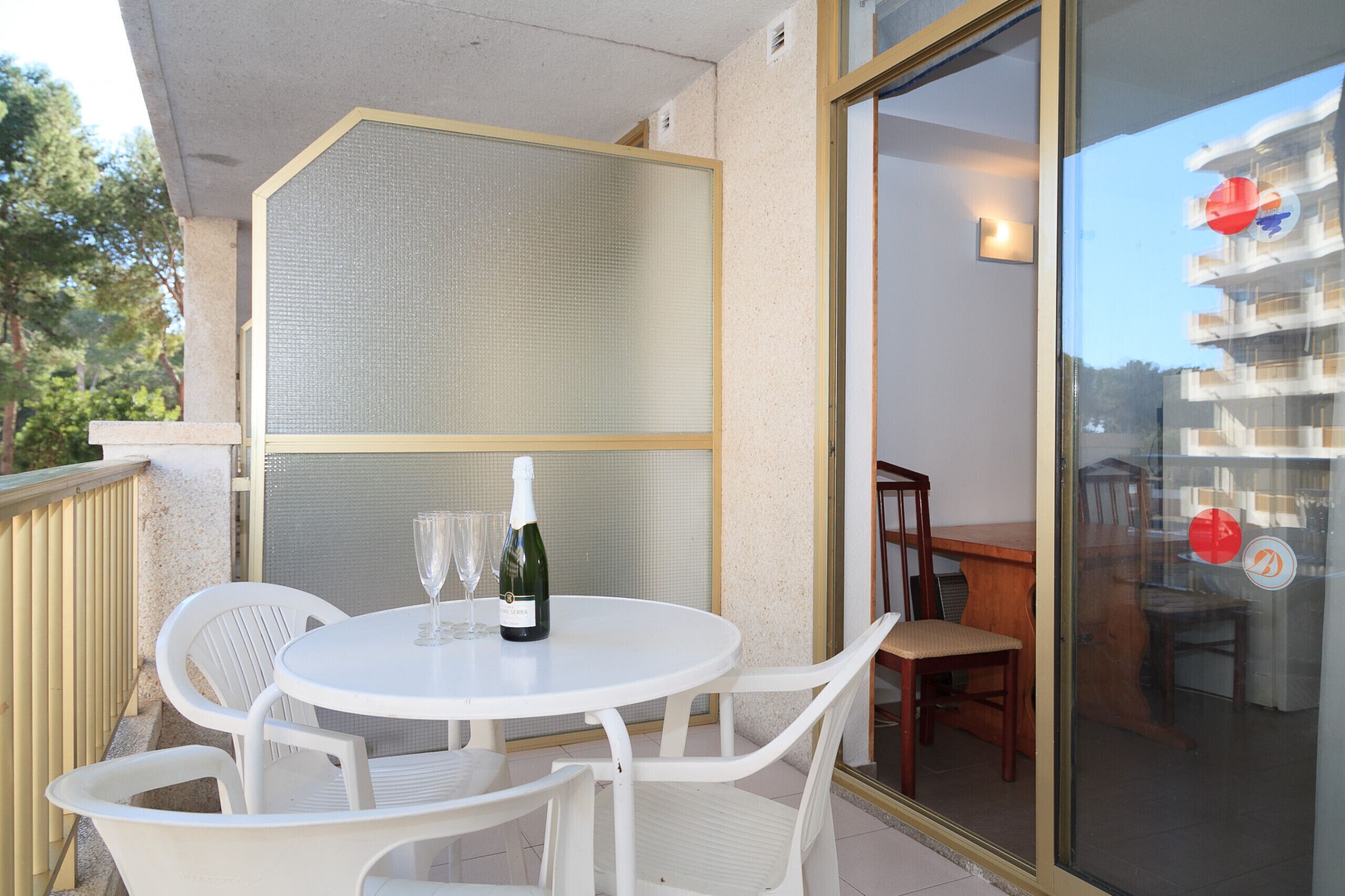 Ein Balkon mit rundem Tisch und weißen Stühlen, einer Champagnerflasche und zwei Gläsern.