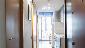 Een gang met houten deuren, een betegelde vloer en zicht op een kamer met een wastafel en kastjes.