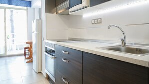 Een moderne keuken met donkerhouten kastjes, een roestvrijstalen spoelbak en een magnetron. Een eethoek met een tafel en stoelen is zichtbaar door een open deur.
