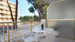 Een balkon met een witte tafel en stoelen, een fles wijn en uitzicht op een gebouw en bomen.