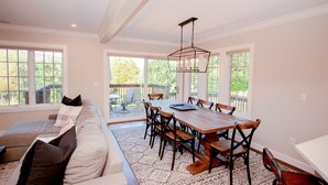 Een eetgedeelte met een houten tafel en stoelen, een bank met kussens, en grote ramen met uitzicht op het omliggende landschap.
