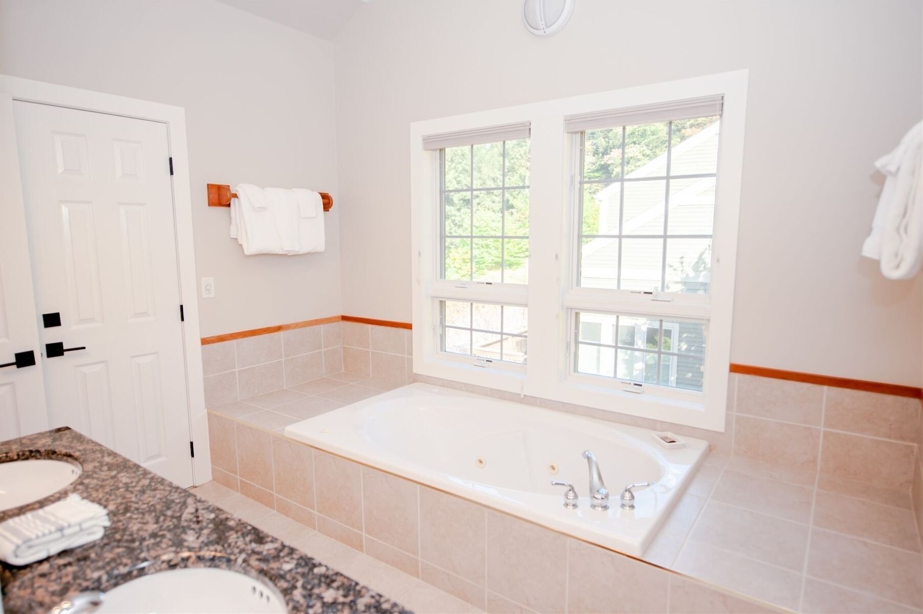 A bathroom with a large bathtub, a sink, and a window with blinds.