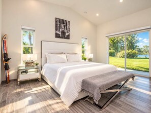 A modern bedroom with a large bed, a ski rack, and a view of a lake.