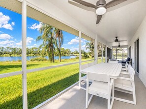 A covered patio with a table and chairs, overlooking a lake and greenery.