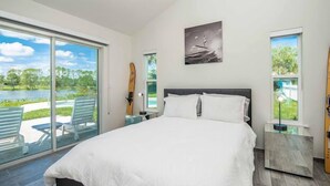 Een slaapkamer met een groot bed, een schuifdeur naar een balkon, een aan de muur hangend schilderij en een nachtkastje met een lamp.