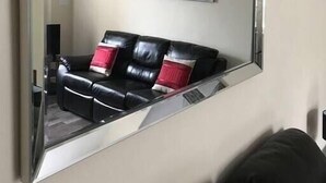 Una sala de estar con un espejo grande, un sofá de cuero negro y un cuadro de un paisaje urbano en la pared.